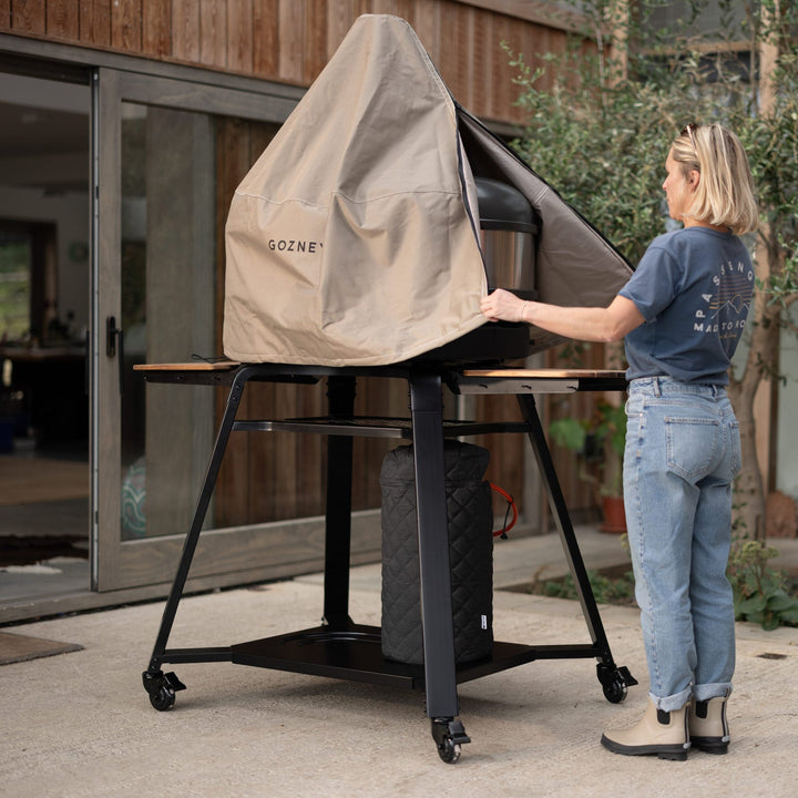 Person setting up a Gozney pizza oven on a stand outdoors.
