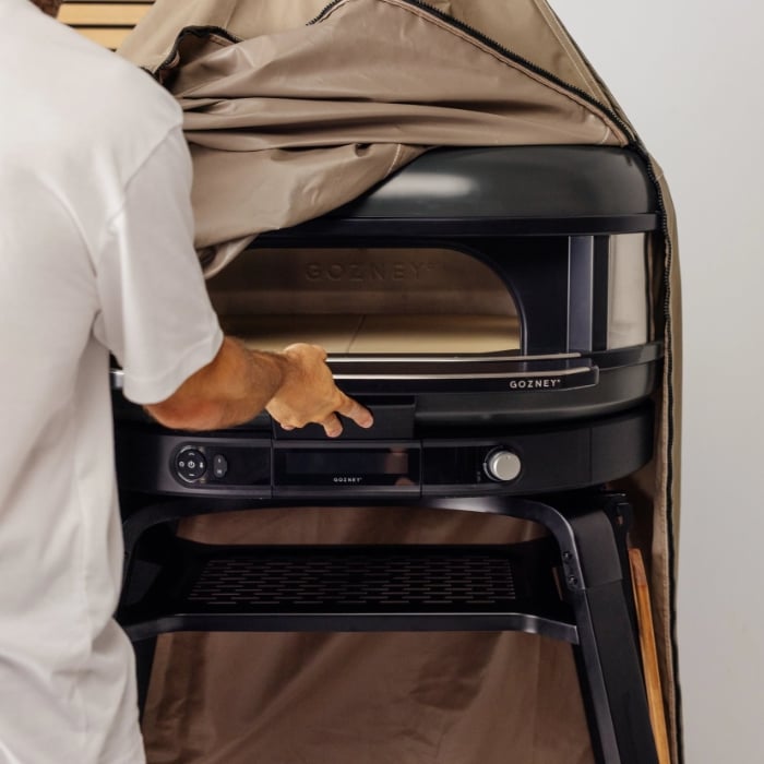 Person removing a beige Gozney cover from a Gozney Dome Gen 2 pizza oven