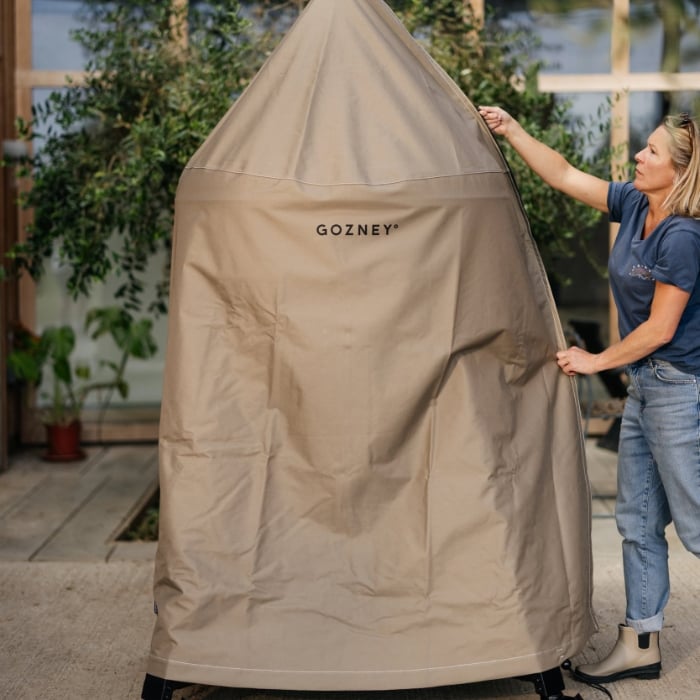 Person holding a beige Gozney grill cover outdoors.