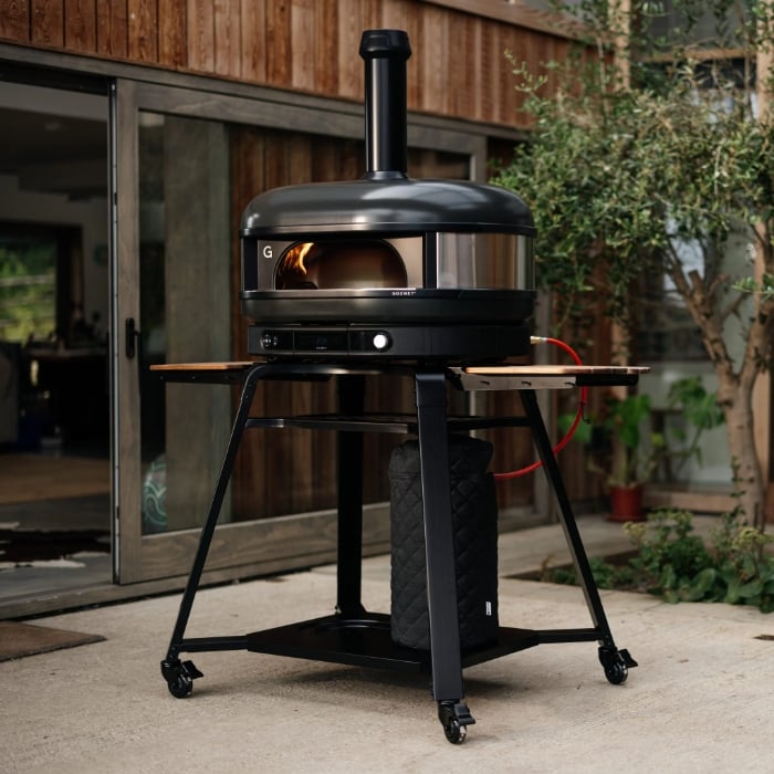 Black outdoor pizza oven on wheels in a backyard setting