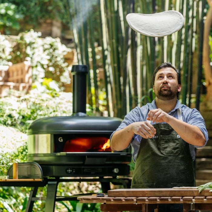 Man preparing pizza outdoors with a portable pizza oven.