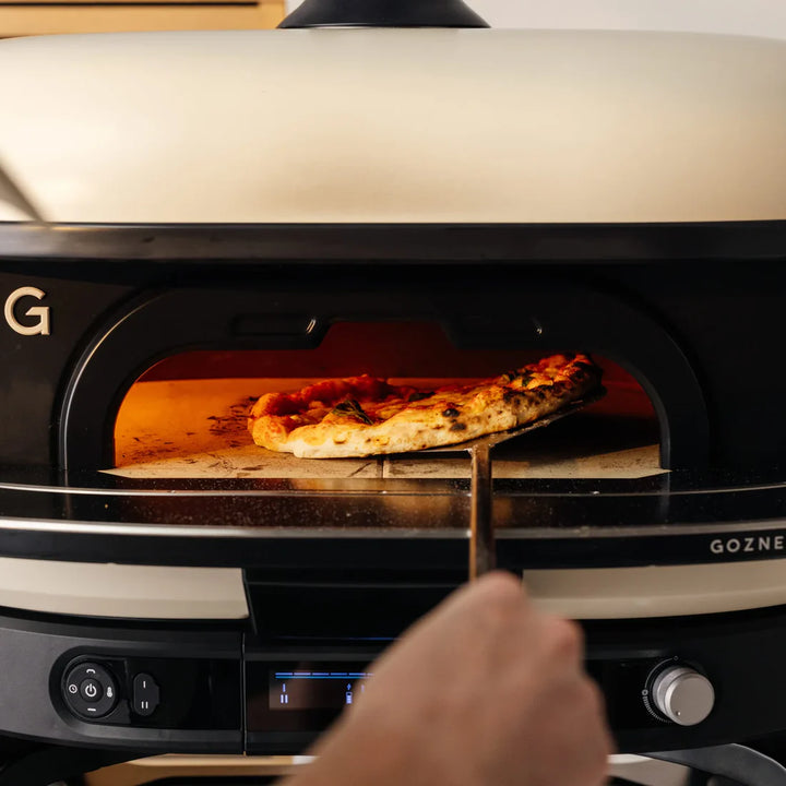 Person taking a pizza out of a GOZNEY pizza oven