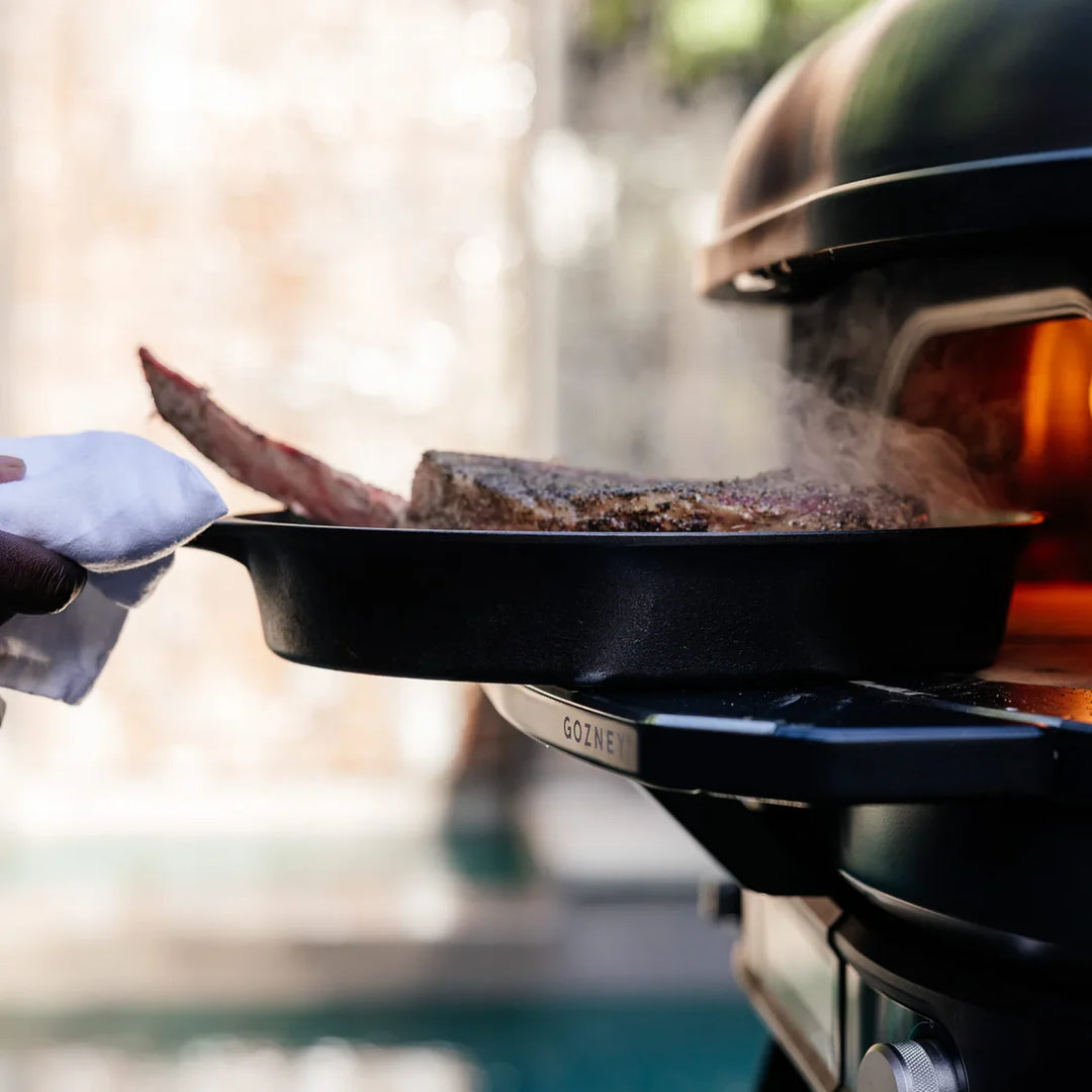 Person grilling meat on a Gozney Dome Gen 2 with a scenic background