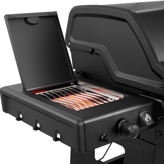 A close-up of a black gas grill with the lid open, showing the interior grates and a basket of food on the side shelf, against a plain white background.