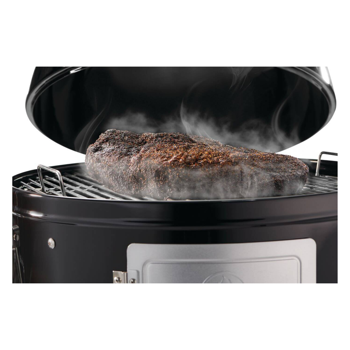 A large cooked steak sits on the grill grate inside a black round smoker or grill, with visible steam rising from the meat against a white background.