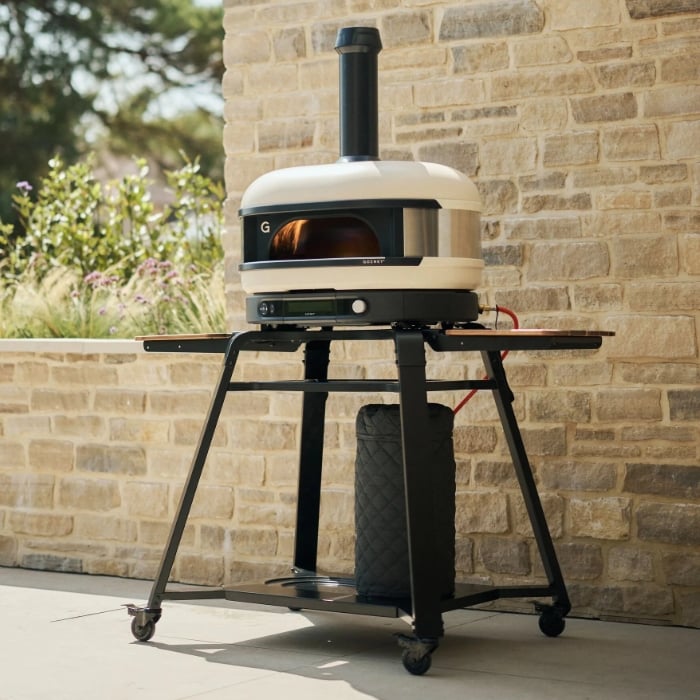 gozney dome gen 2 pizza oven on a stand outdoors against a brick wall.